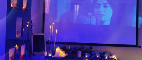 A room with a large screen displaying a projection, a seating area with candles, and a blue-lit ambiance.