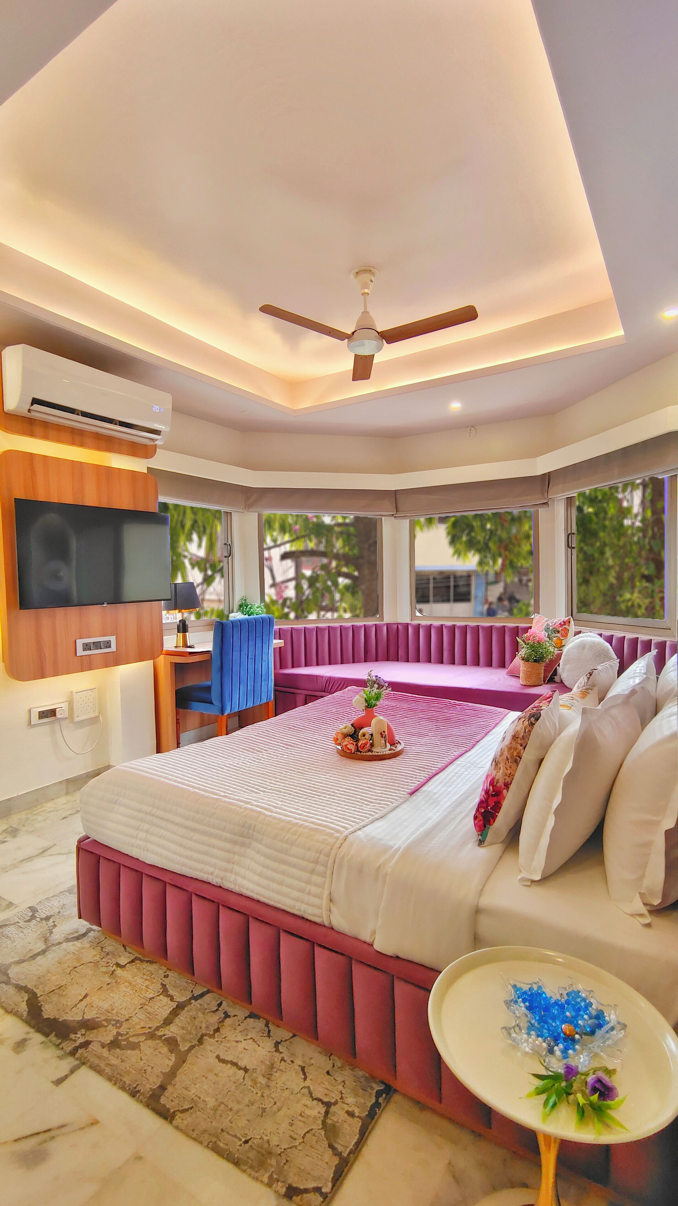 A modern bedroom with a large bed, a TV mounted on the wall, and a ceiling fan.