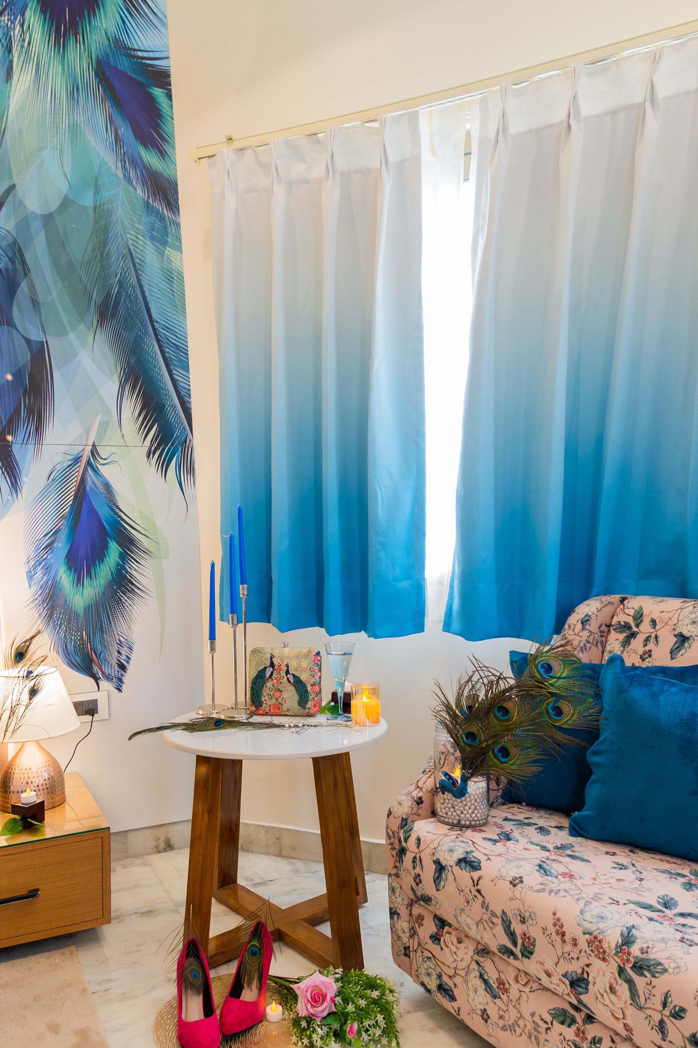 A room with a floral sofa, a round wooden table, and a peacock feather decoration.