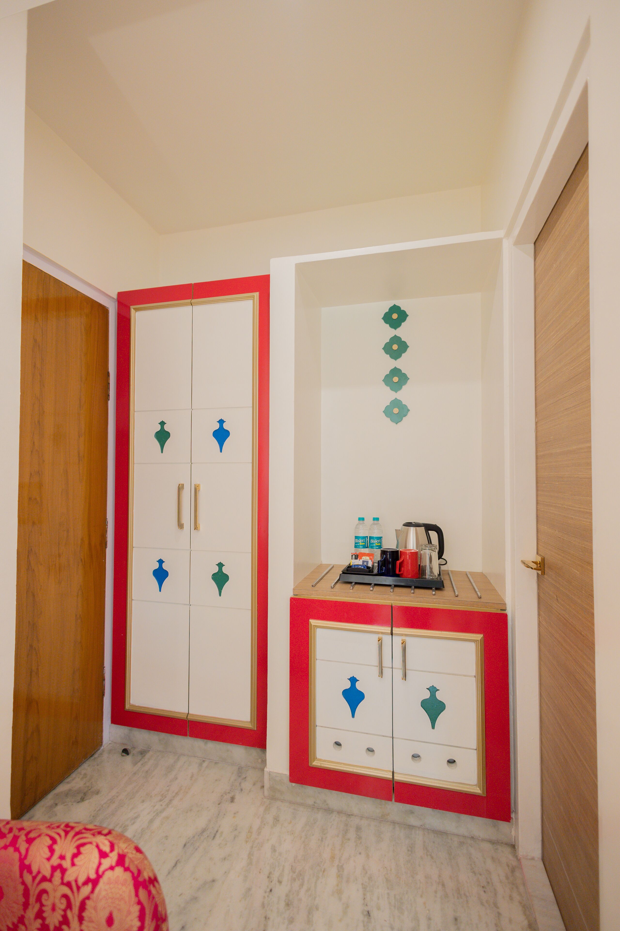 A room with a wardrobe featuring a red and white color scheme, a small table with a kettle and water bottles, and a patterned chair.