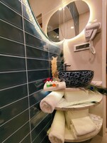 Un baño con pared de azulejos negros, un lavabo redondo con un cuenco decorativo y un secador de pelo fijado a la pared.