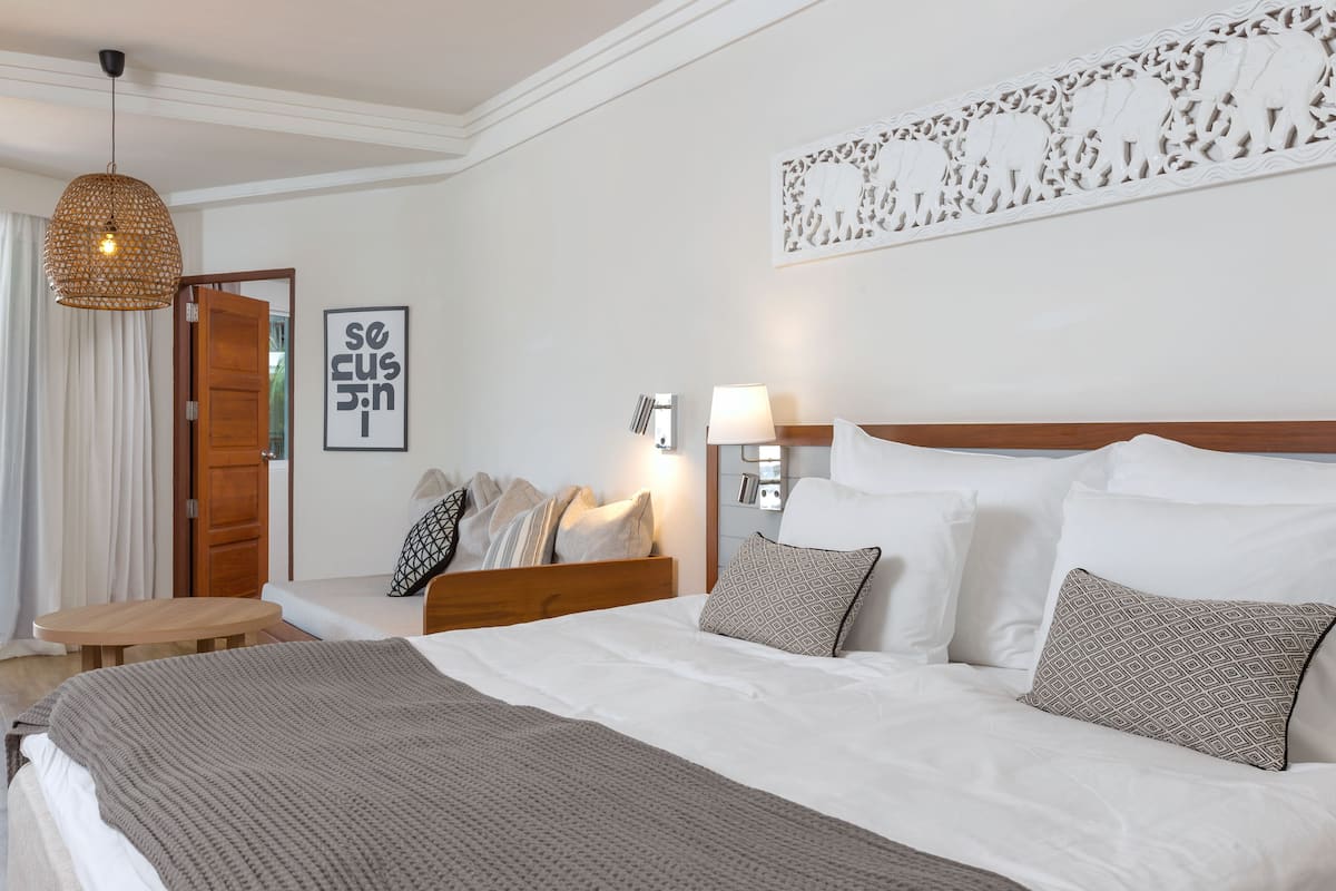 Une chambre à coucher bien aménagée, avec un grand lit, des tables de chevet, un luminaire suspendu et une œuvre d’art accrochée au mur.