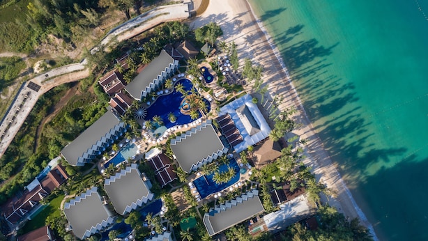 Vista aérea de un resort con varias piscinas, una playa y palmeras.