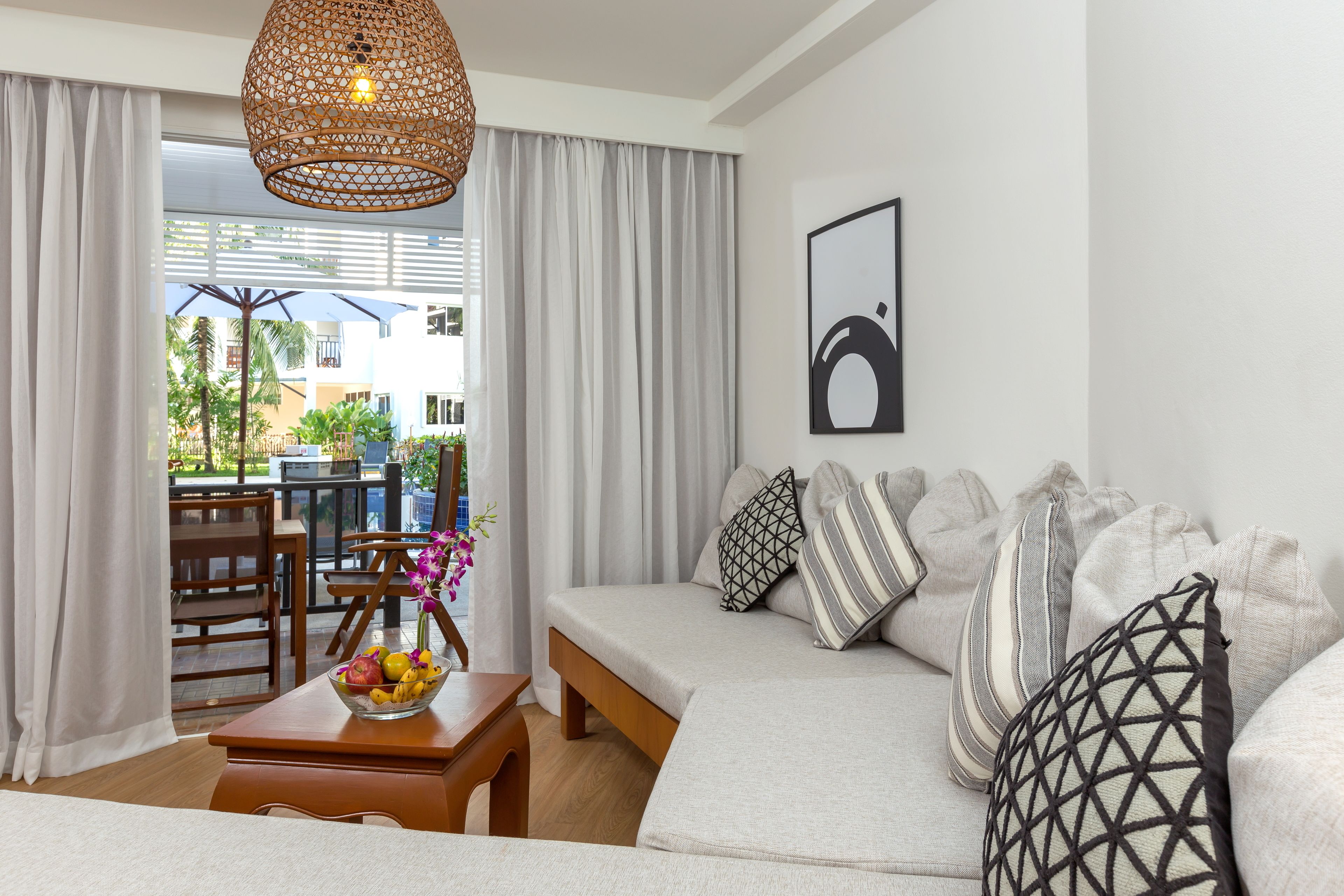 A modern living room with a sofa, a dining table with chairs, a hanging light fixture, and a view of the outdoors.