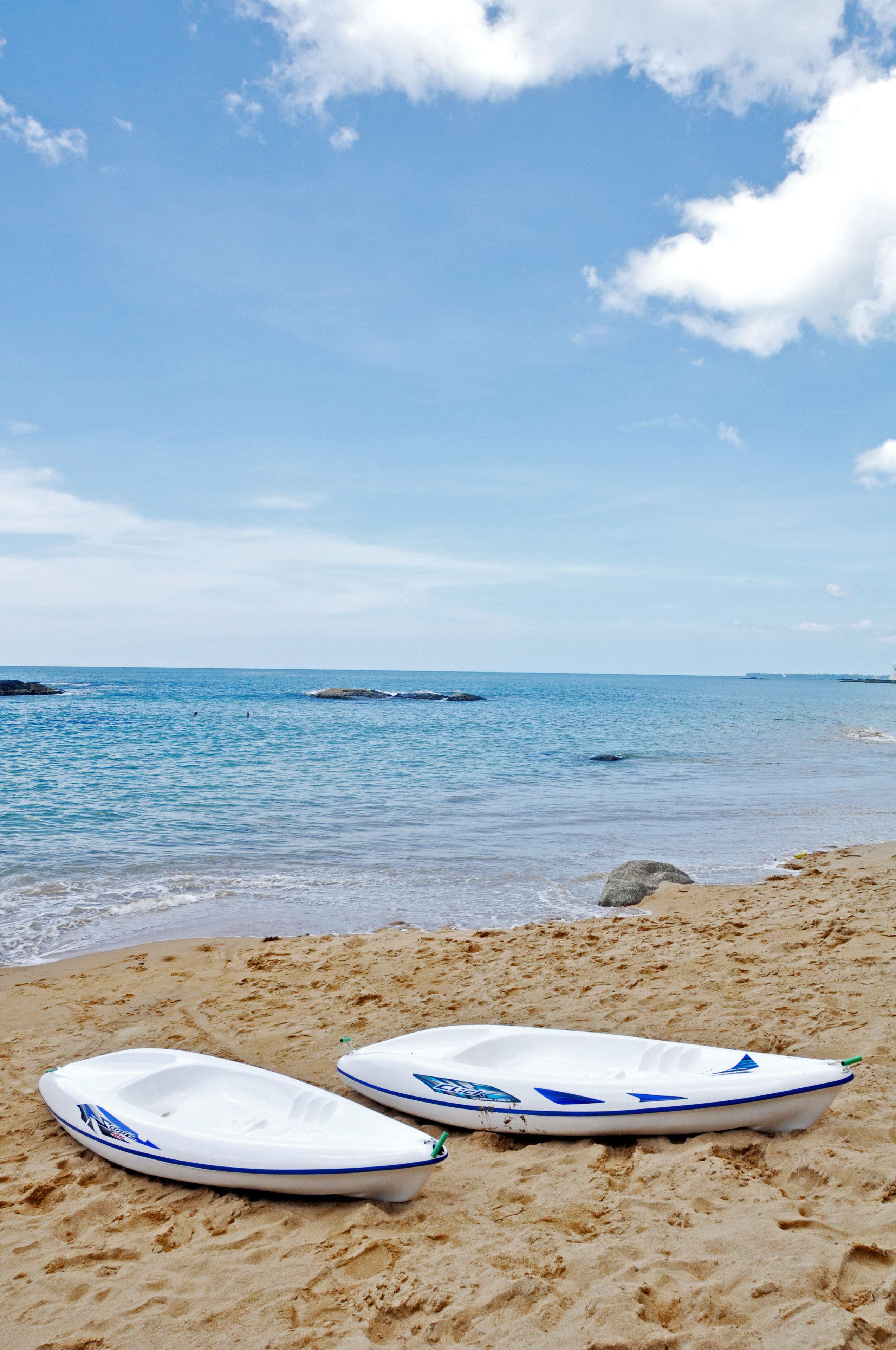 Two white boats on a sandy beach with a clear blue sky and calm sea.