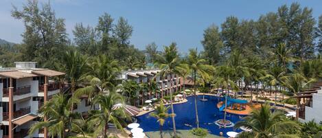 A resort with a large central pool surrounded by palm trees and multiple buildings with balconies.