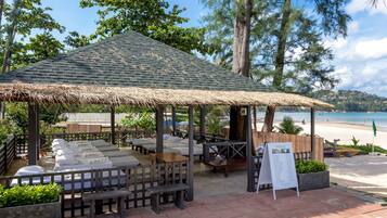 A beachside massage area with wooden furniture and a thatched roof, overlooking the beach.