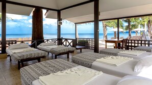 Habitación de hotel frente a la playa con cuatro camas, una mesa de madera y vista al océano.
