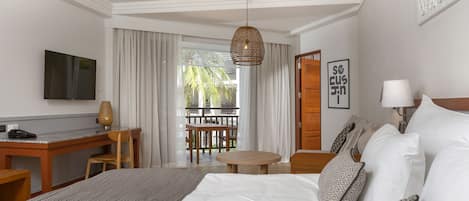 A hotel room with a large bed, a desk, a television, and a balcony with a view of palm trees.