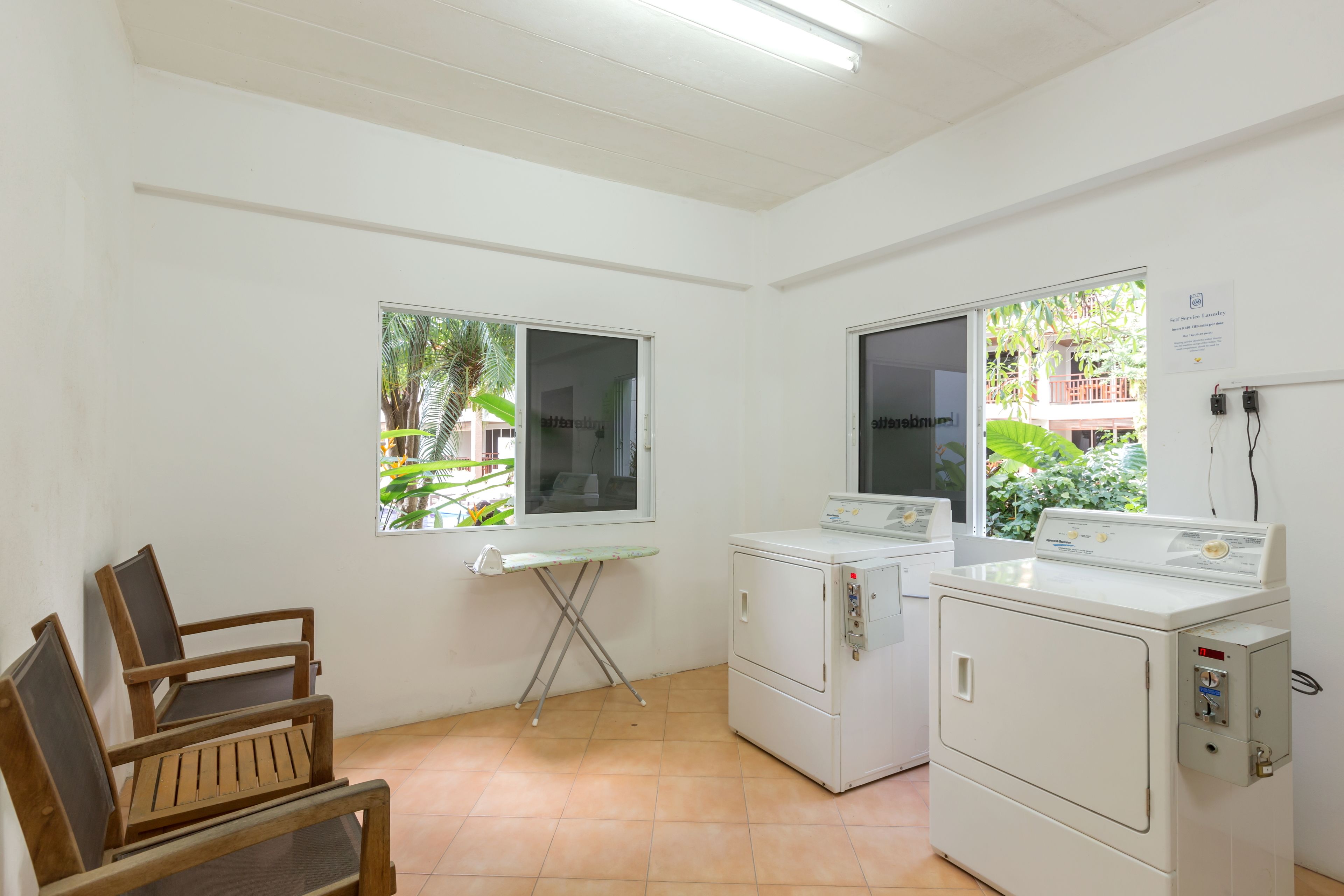A laundry room with two washing machines, a folding table, and wooden chairs.