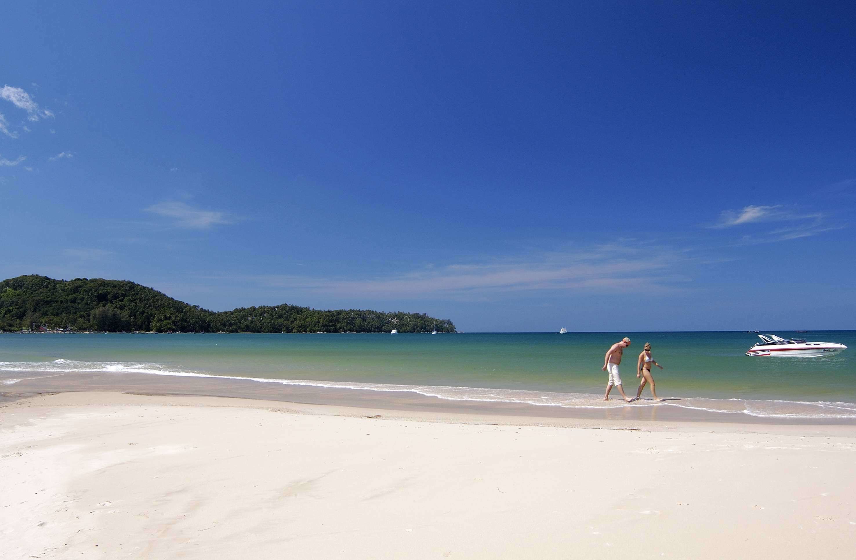 Una playa con un bote en el agua y una persona caminando por la orilla.