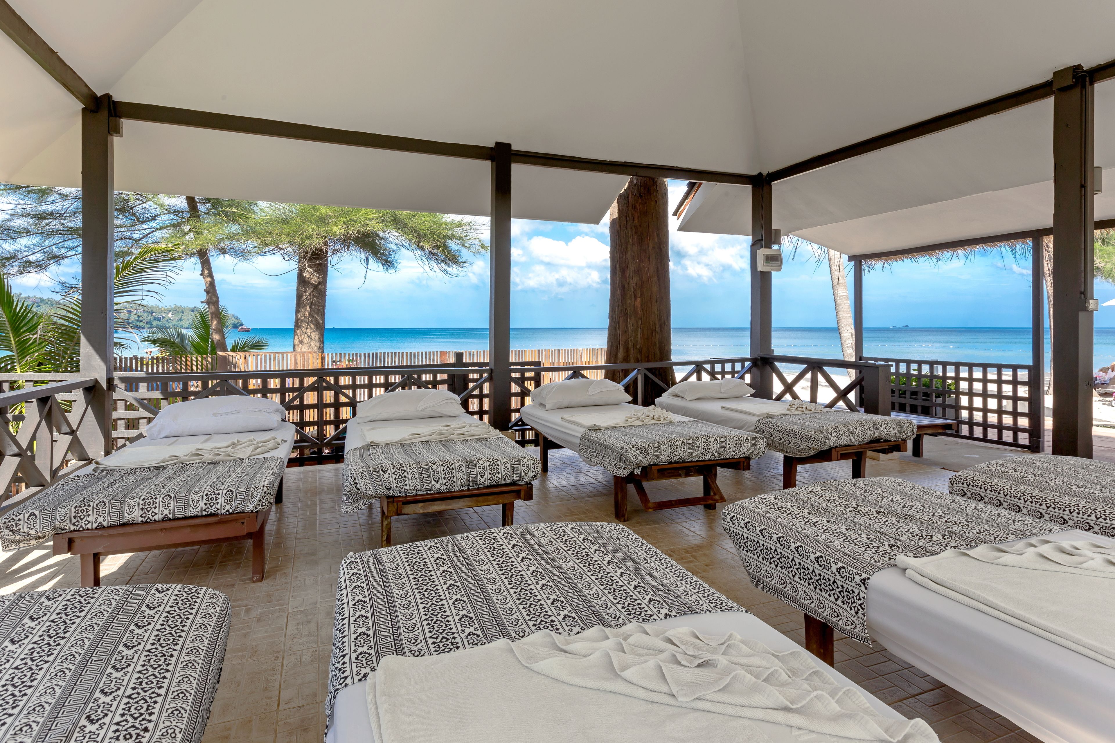 Un espace extérieur aménagé, abrité et doté de plusieurs lits, chacun agrémenté d’une literie à motifs, avec vue sur une plage.