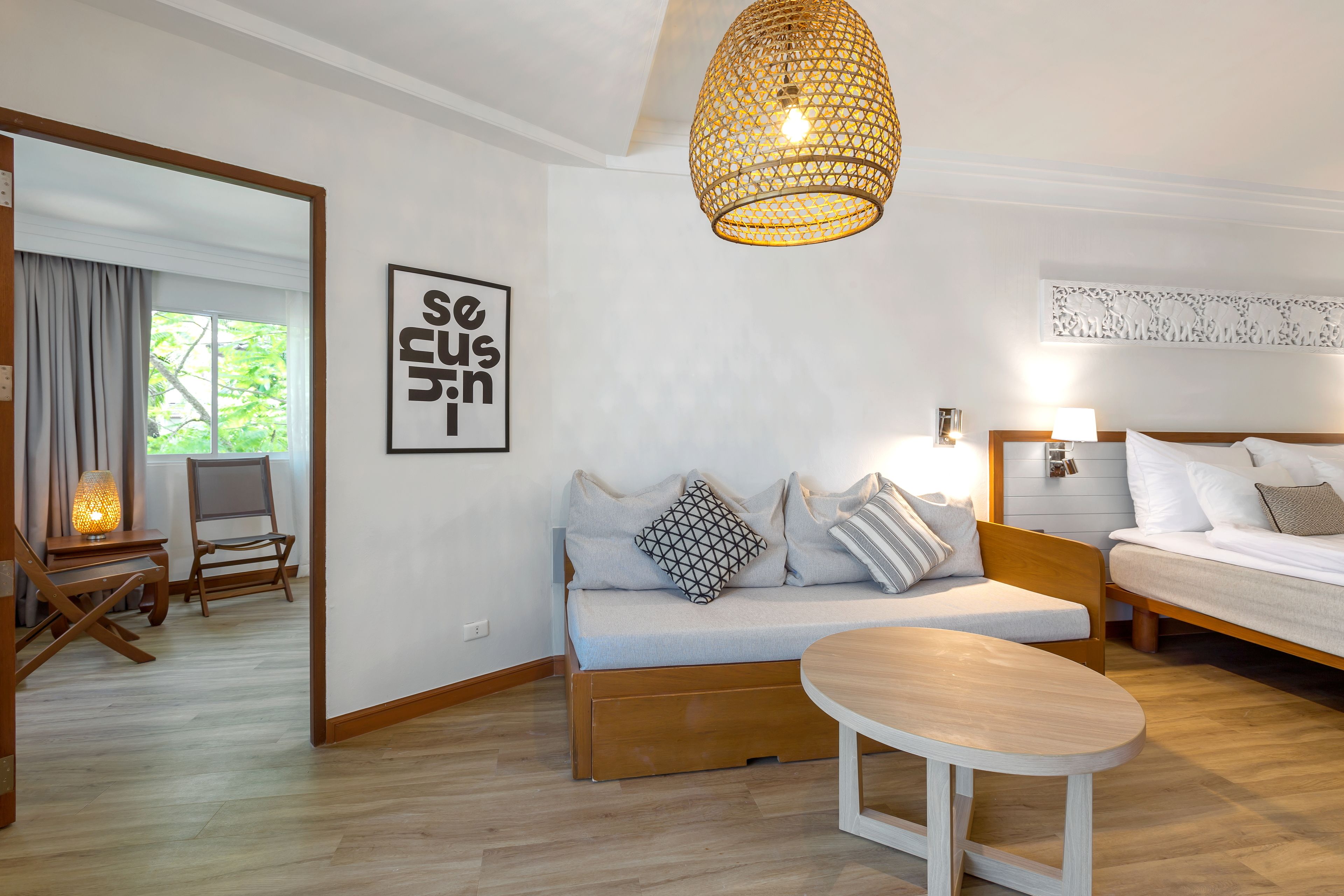 A modern hotel room with a sofa, a bed, a small table, and a hanging light fixture.