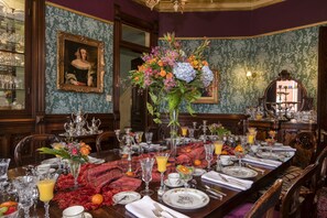 A formal dining room with a long table set for a meal, surrounded by ornate wallpaper and classic furniture. - The Empress of Little Rock (Little Rock)