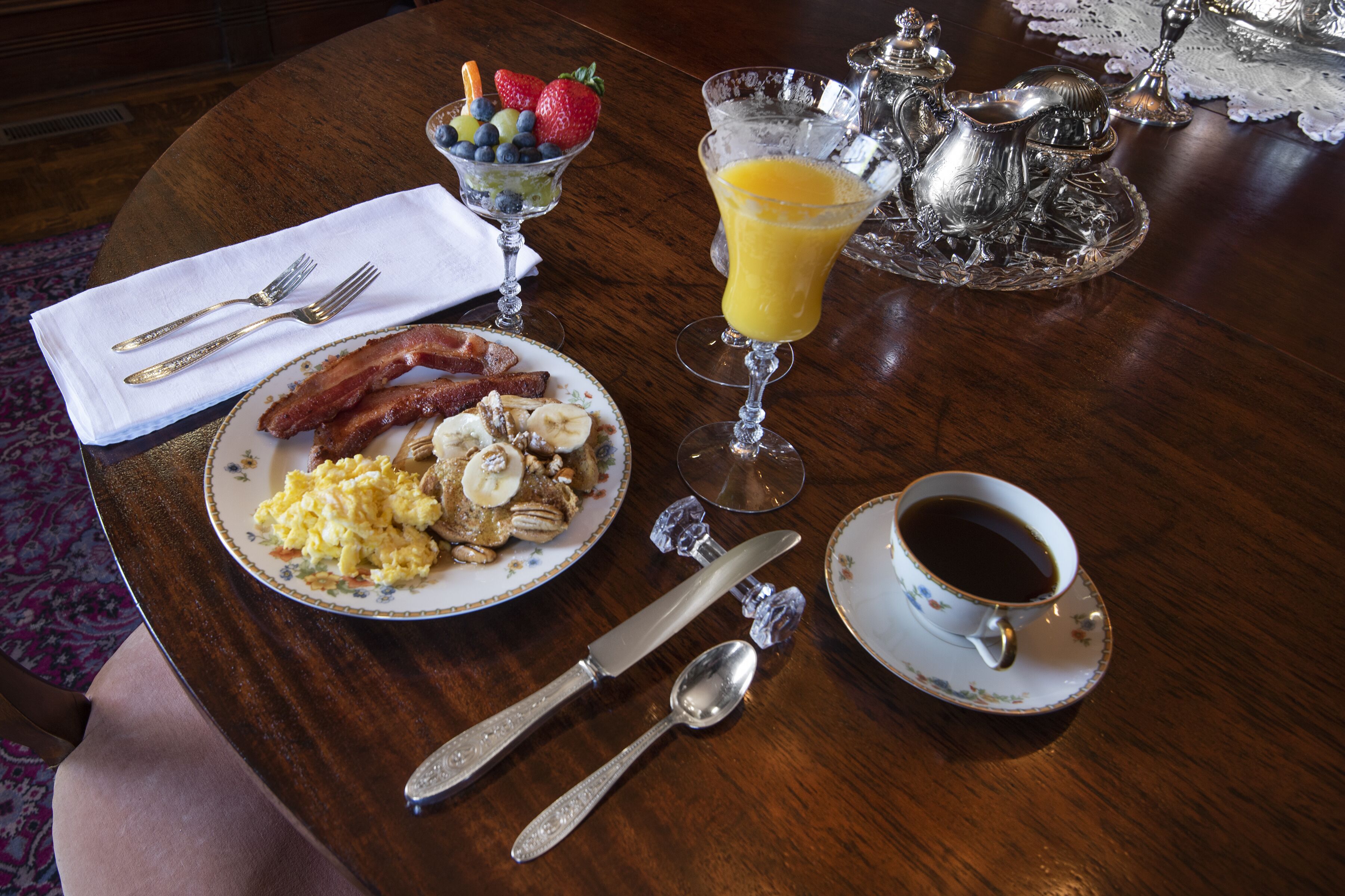 Una mesa de desayuno con huevos, tocino y fruta, un vaso de jugo de naranja y una taza de café.