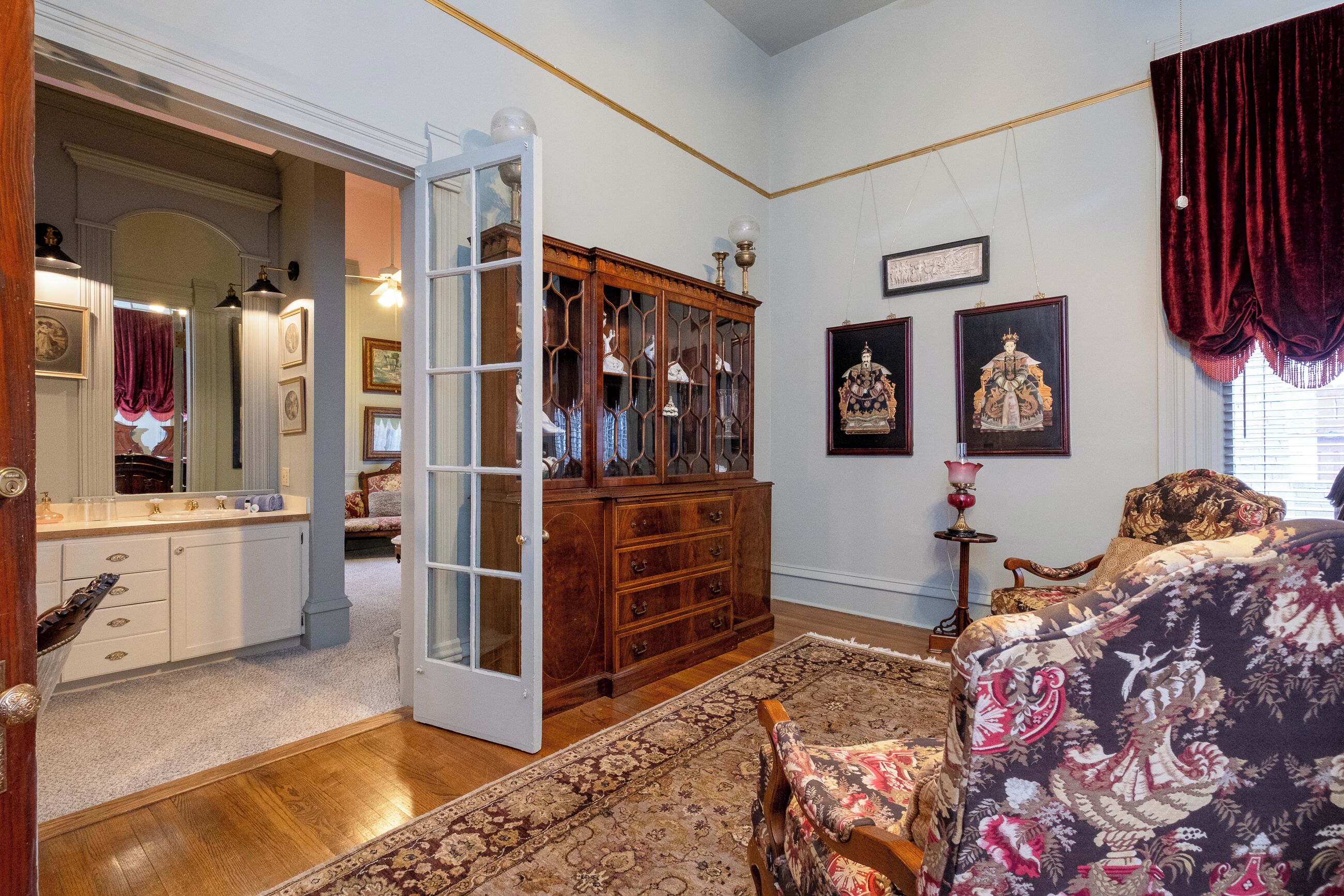 A room with a wooden dresser, a mirror, a patterned rug, and a bed with a floral bedspread.