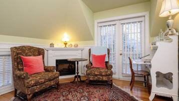 A living room with two armchairs, a fireplace, a dining table, and a white cabinet.