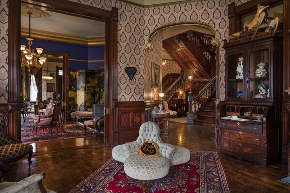 Una amplia sala con un sillón grande, una escalera y un aparador de madera con adornos.