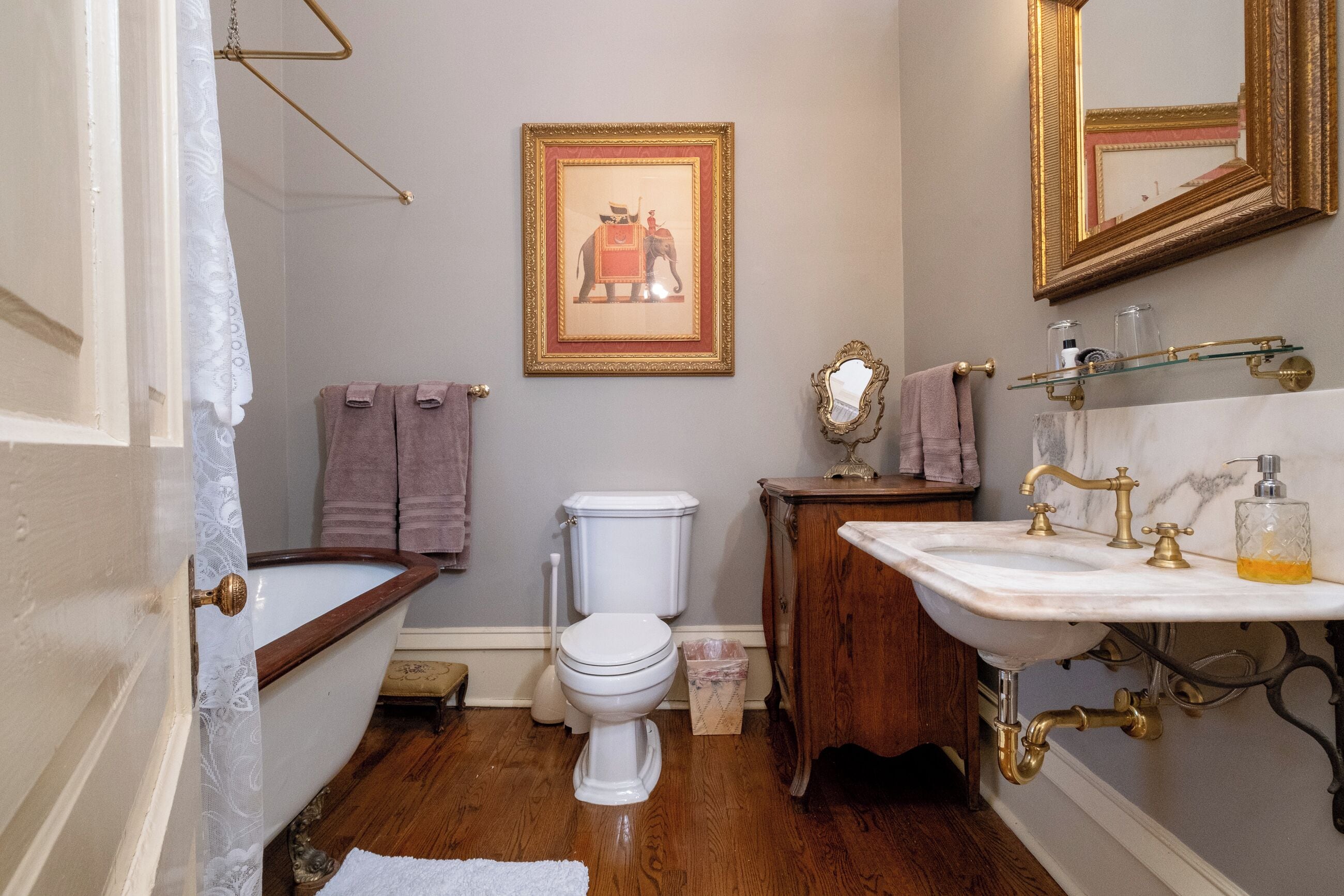 A bathroom with a toilet, sink, and bathtub. There is a framed picture on the wall and a towel rack with towels.