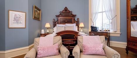 A bedroom with a large bed, two armchairs, a dresser, and a window with curtains.