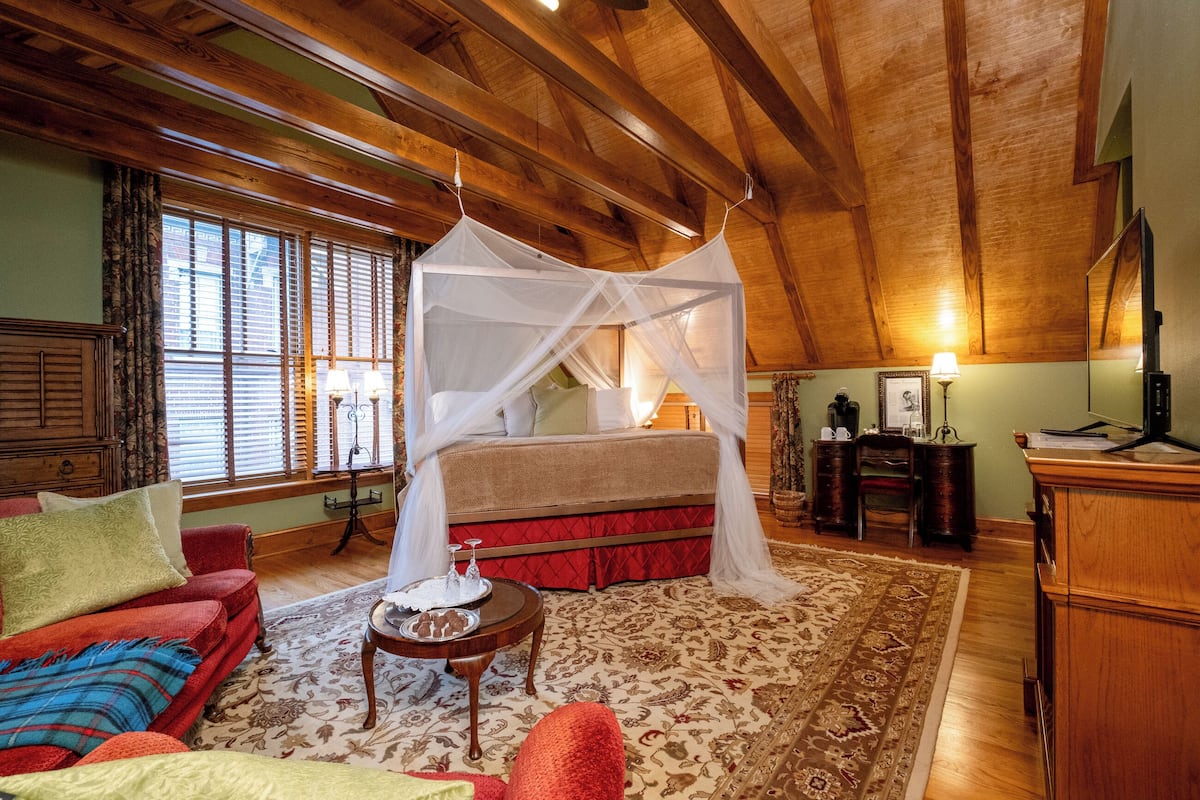 Une chambre à coucher avec un lit à baldaquin, un canapé rouge, une petite table avec un plateau, et un plafond en bois.