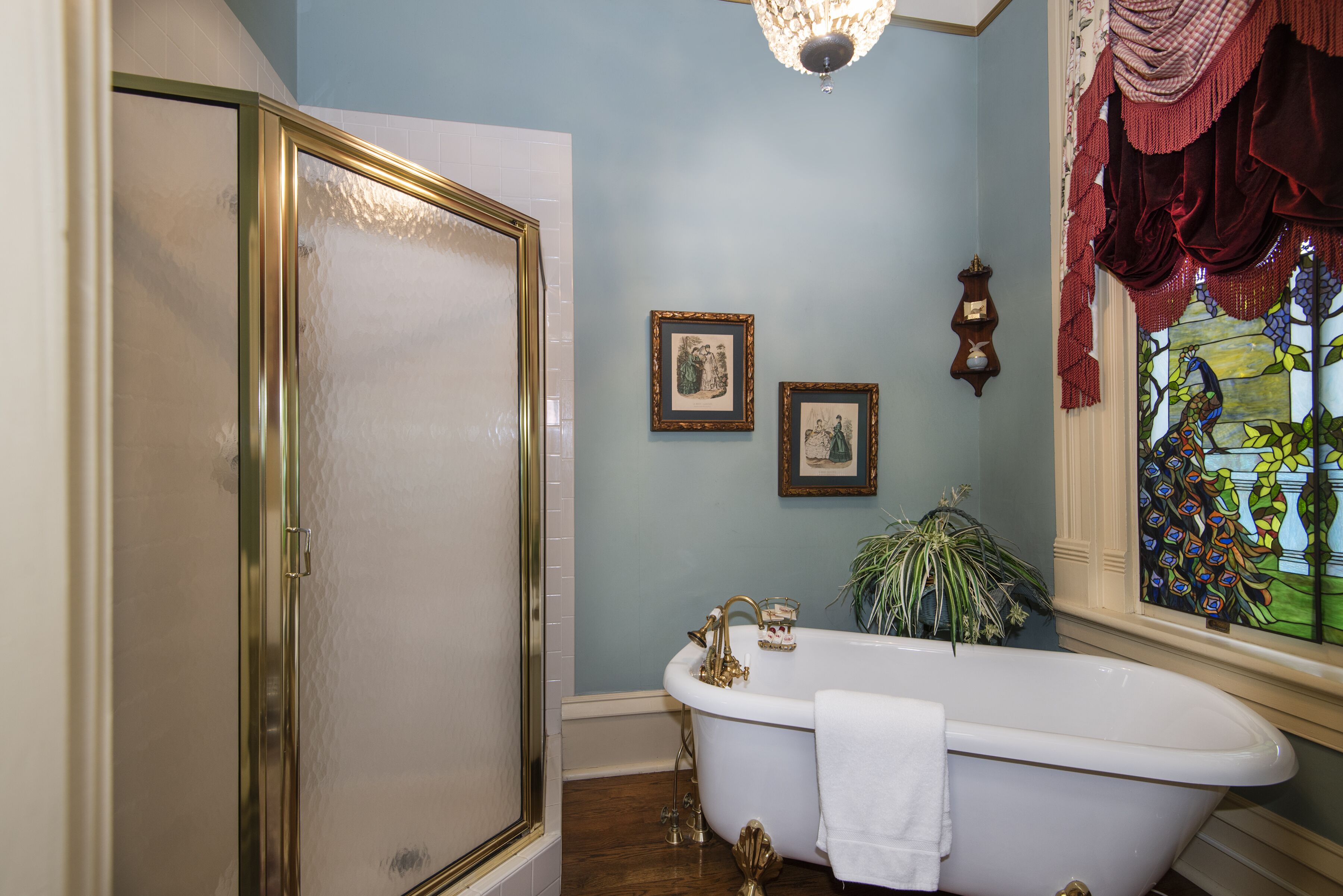 A bathroom with a clawfoot bathtub, a shower with a gold frame, and a stained glass window.