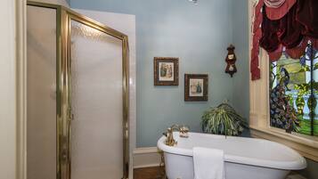 A bathroom with a clawfoot bathtub, a shower with a gold frame, and a stained glass window.