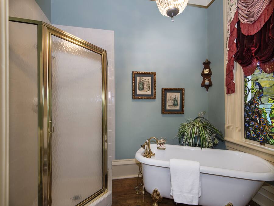 A bathroom with a clawfoot bathtub, a shower with a gold frame, and a stained glass window.