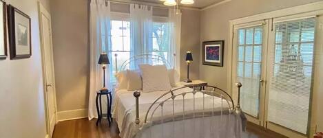 Une chambre avec un lit en métal, un ventilateur de plafond et une fenêtre avec des rideaux.