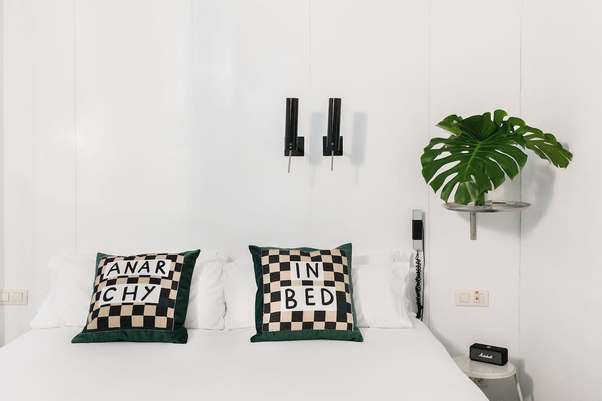 A bed with two pillows, a plant, and a small table with a speaker.