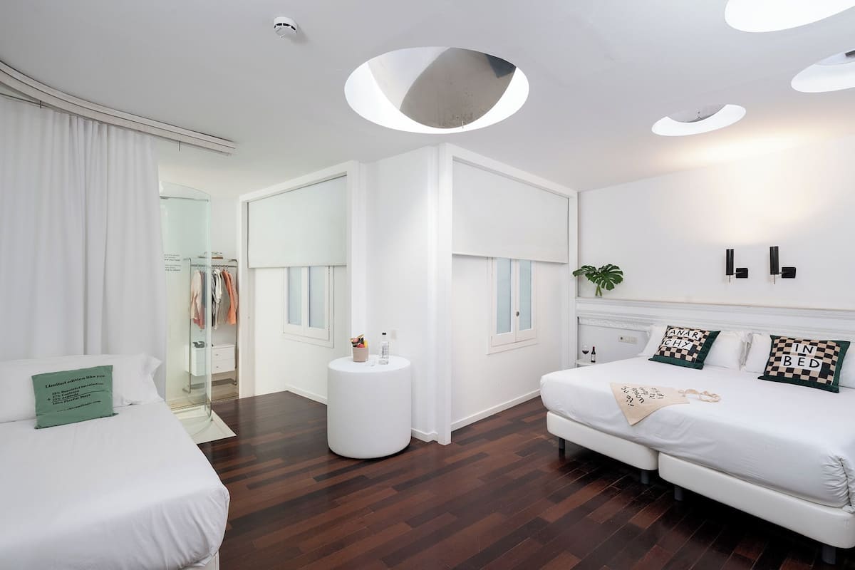 A modern bedroom with a large bed, a smaller bed, a round white side table, and a wardrobe.