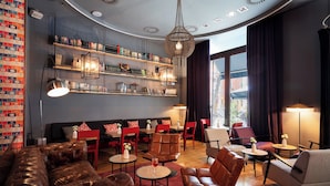 A modern lounge area with leather sofas, red chairs, and a bookshelf filled with books and decorative items. - Chic&Basic Born Boutique Hotel (Barcelona)