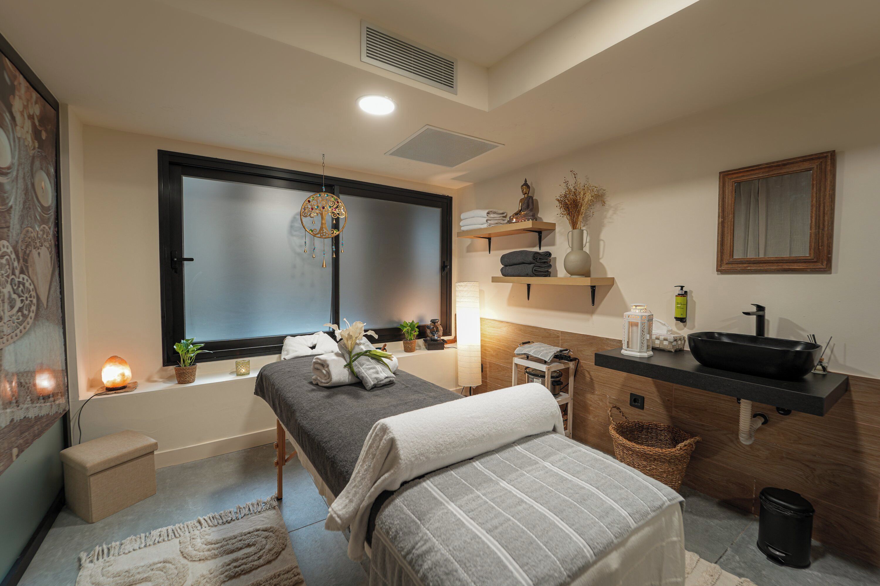 Un dormitorio moderno con cama, mesita de noche, ventana y baño con lavamanos y espejo.