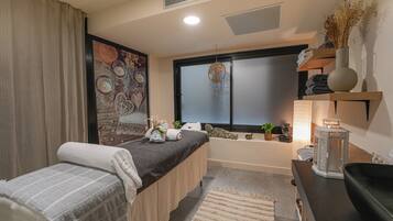Una habitación con cama, ventana, estante con objetos decorativos y mesita de noche.