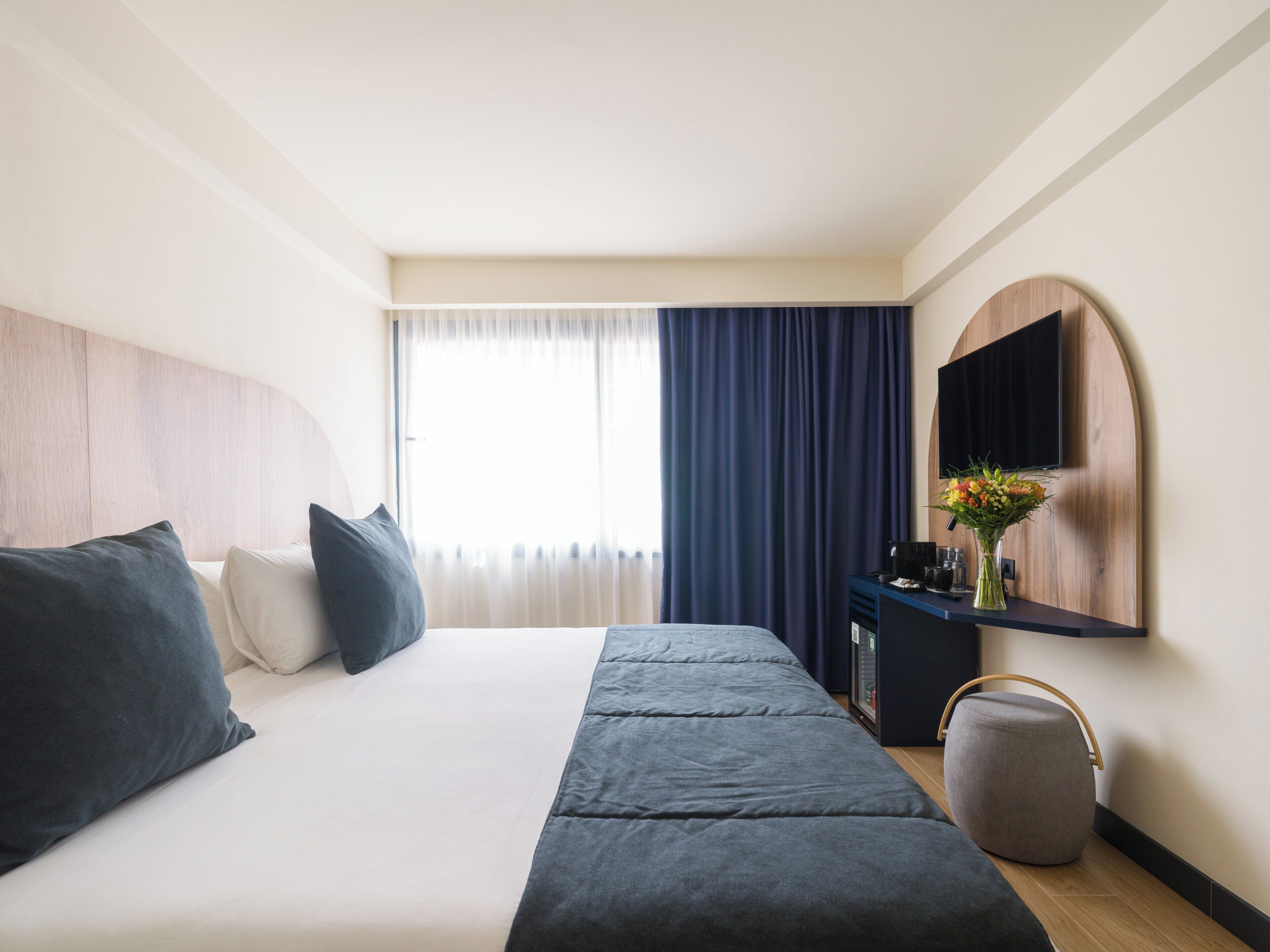 A hotel room with a bed, a desk, a chair, a TV, and a window with curtains.