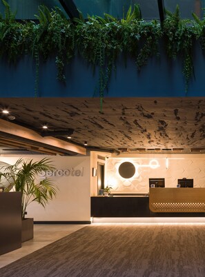 Ein Hotel-Empfangsbereich mit modernem Design, inklusive einer Rezeption, eines großen Topfpflanzens und einer Wandpflanzenanordnung.