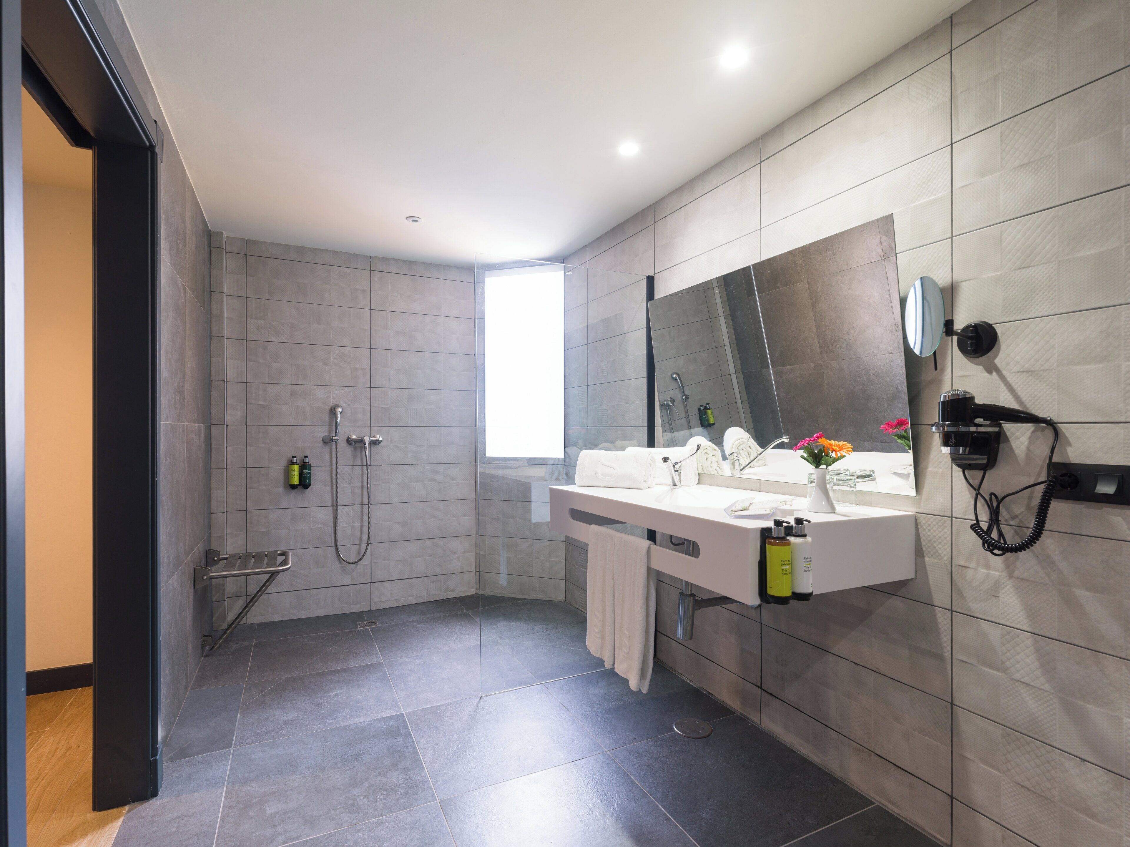 A modern bathroom with a shower, a large mirror, and a hairdryer mounted on the wall.