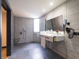 Un baño moderno con ducha, un espejo grande y un secador de pelo montado en la pared.