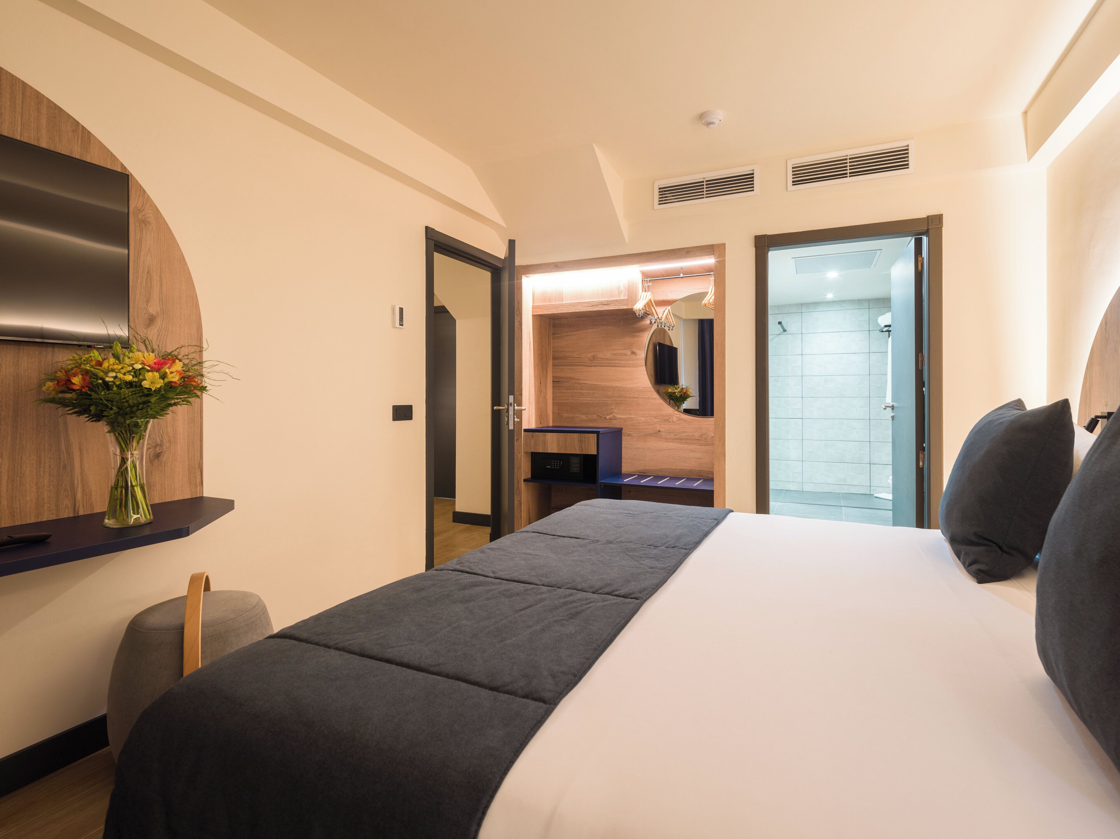 Habitación de hotel con cama, escritorio, espejo, ducha y un florero con flores.