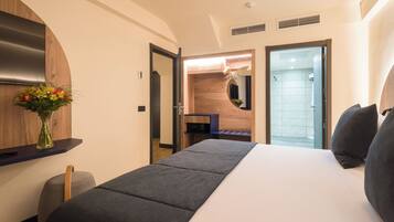 Une chambre d’hôtel avec un lit, un bureau, un miroir, une douche et un vase avec des fleurs.