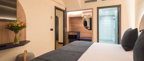 Habitación de hotel con cama, escritorio, espejo, ducha y un florero con flores.
