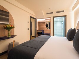 A hotel room with a bed, a desk, a mirror, a shower, and a vase with flowers.