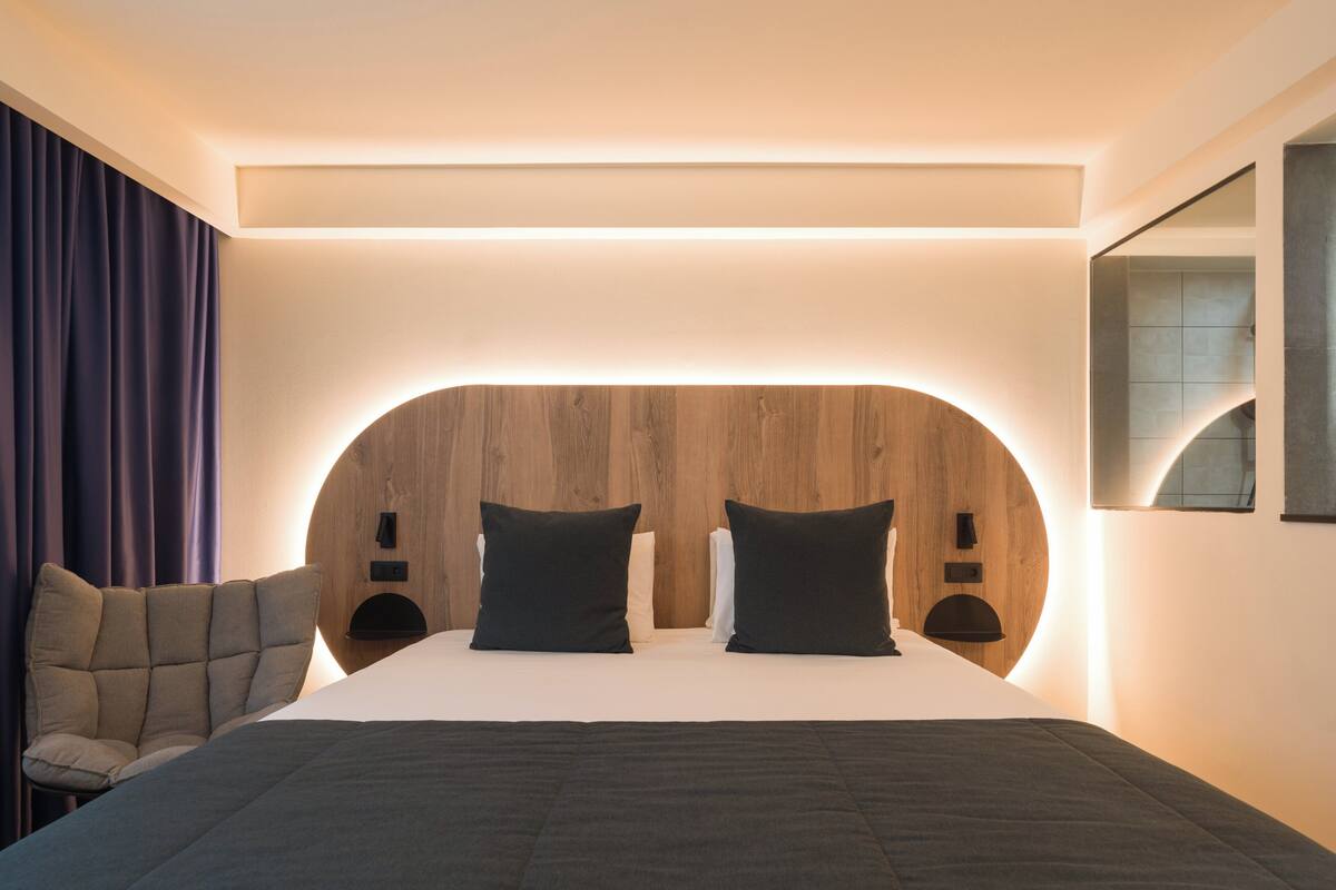 Una habitación de hotel moderna con una cabecera curvada, una cama grande, una silla y un espejo en la pared.