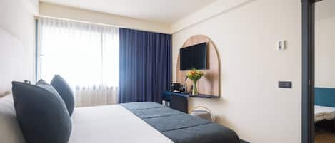 A hotel room with a bed, a desk, a mirror, and a view of another room.