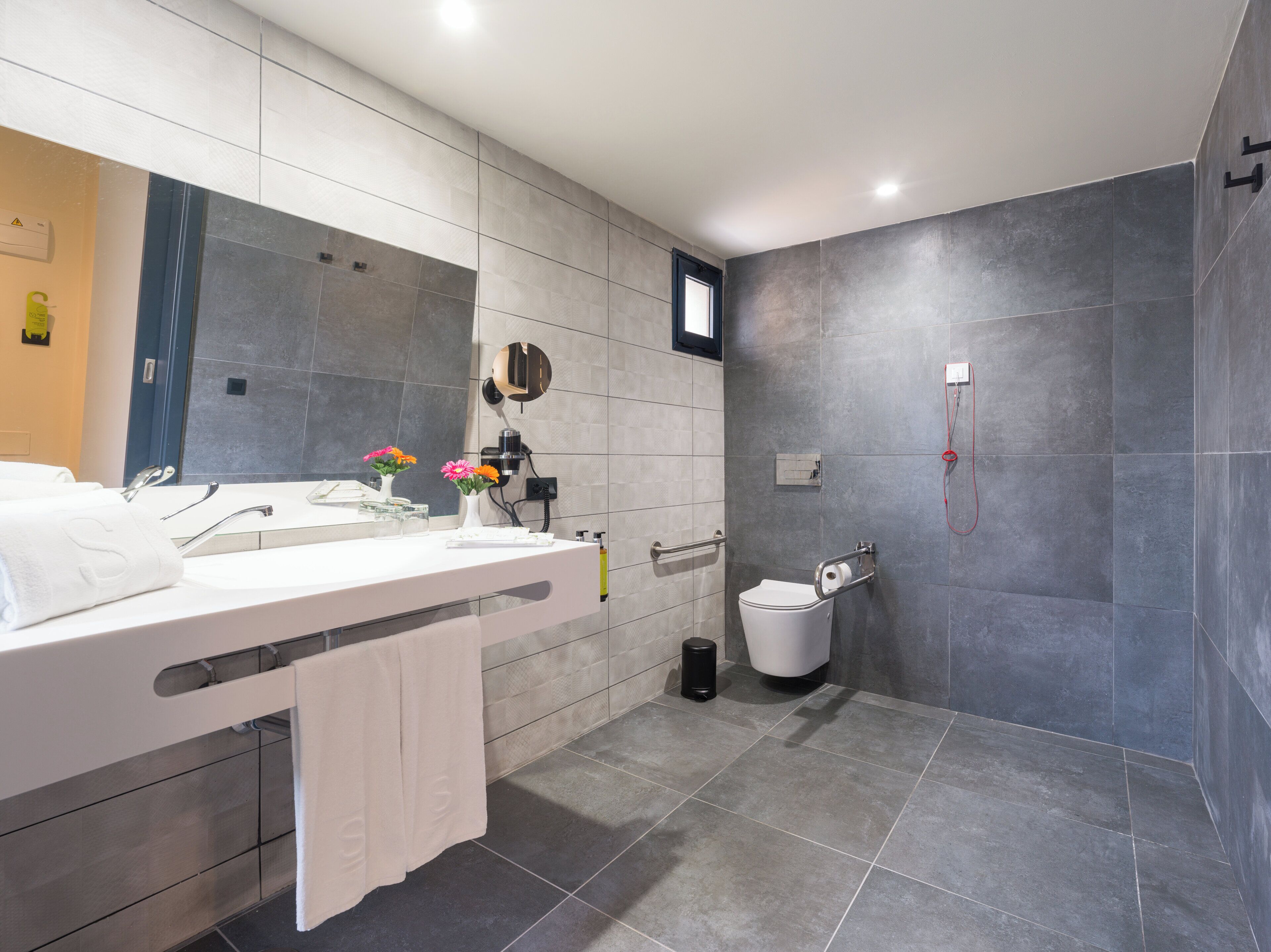 Un baño moderno con un espejo grande, tocador con lavamanos, inodoro y zona de ducha.