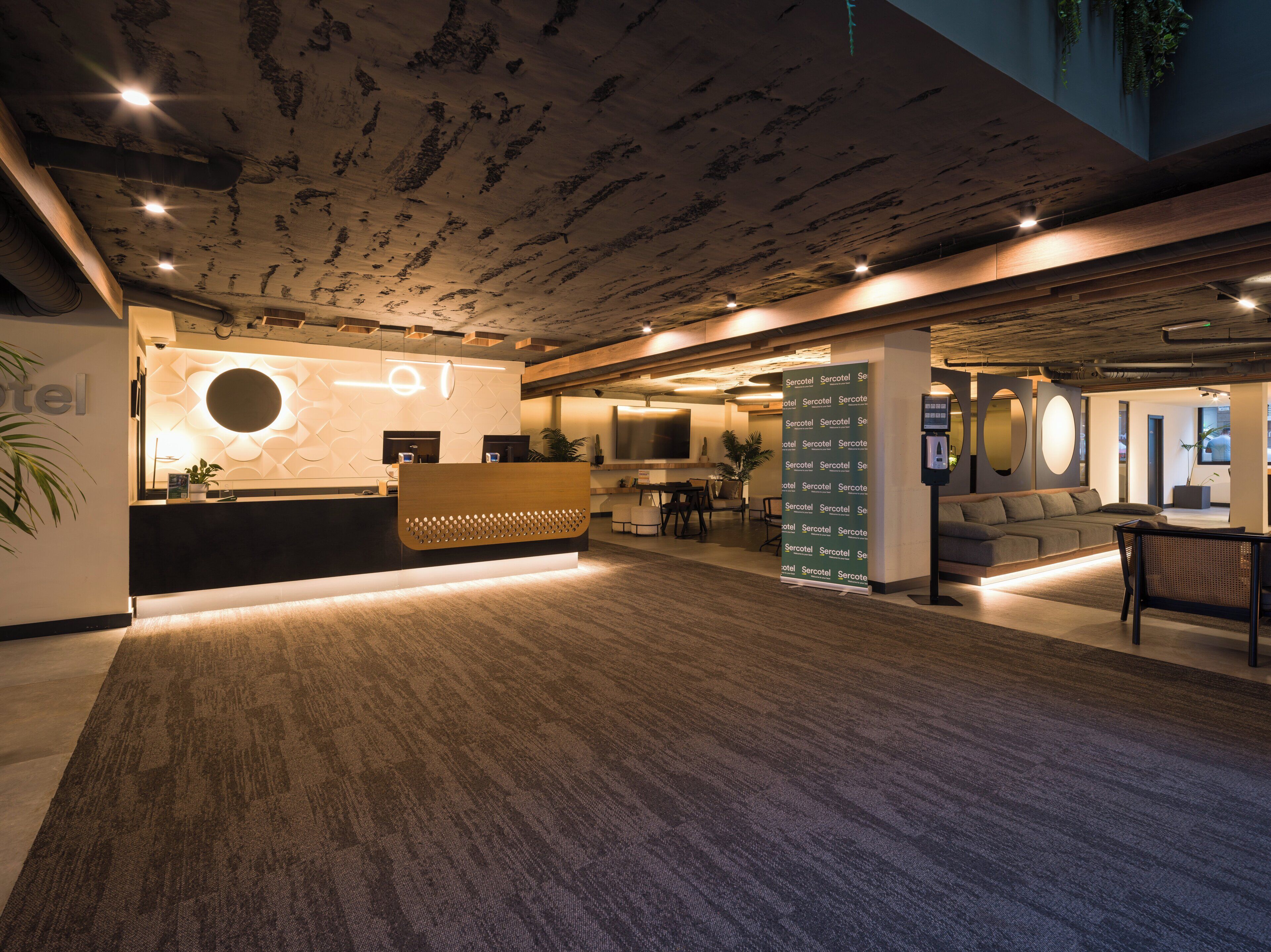 A hotel reception area with a modern design, including a reception desk, seating area, and a wall-mounted directory.