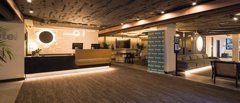 A hotel reception area with a modern design, including a reception desk, seating area, and a wall-mounted directory.
