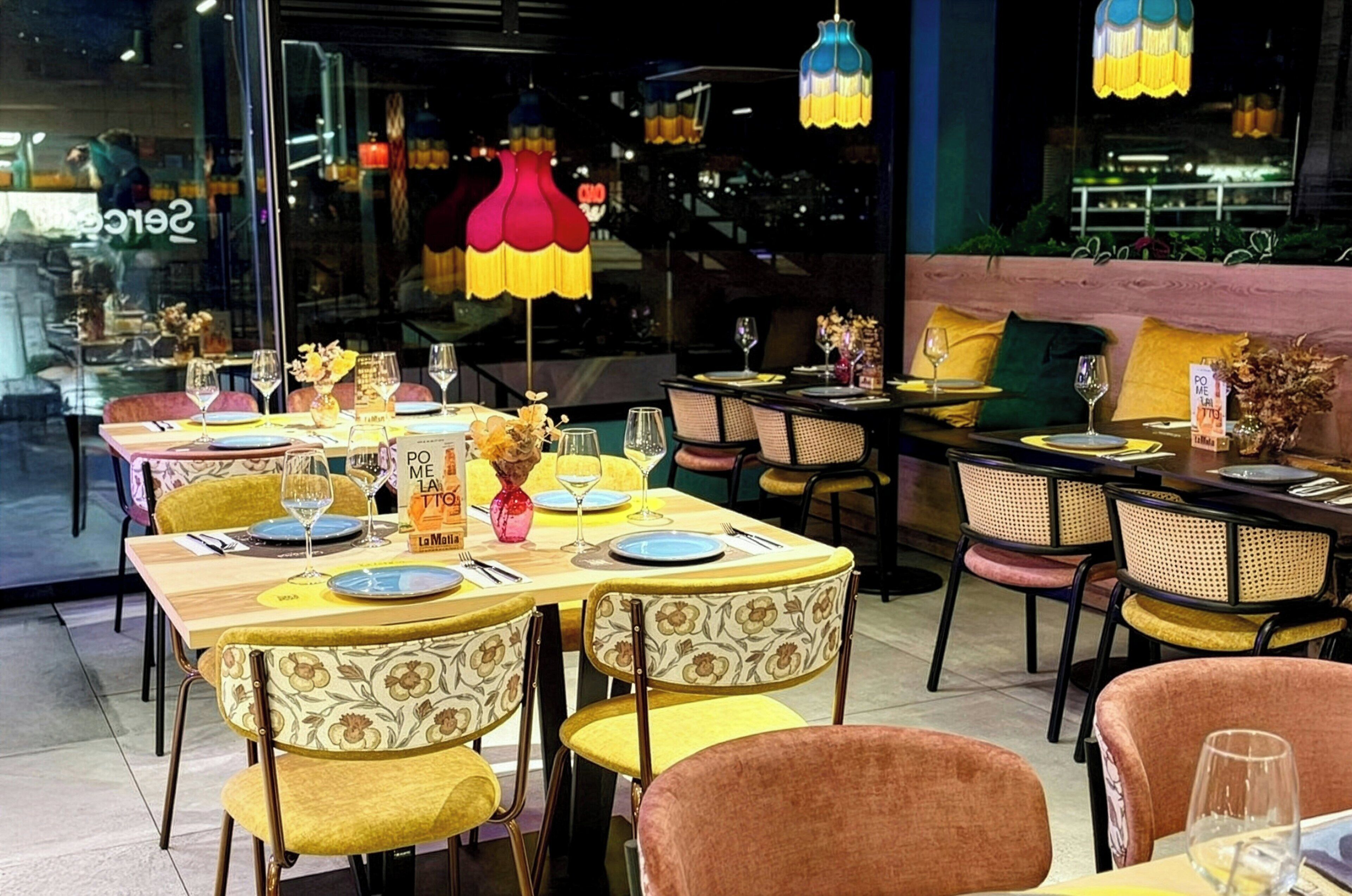 Un restaurante con mesas dispuestas para comer, sillas con tapicería floral y lámparas colgantes.