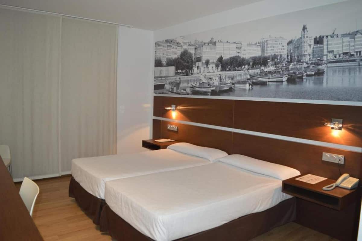 Habitación de hotel con dos camas, un mural con vista urbana en la pared y cabecera de madera.