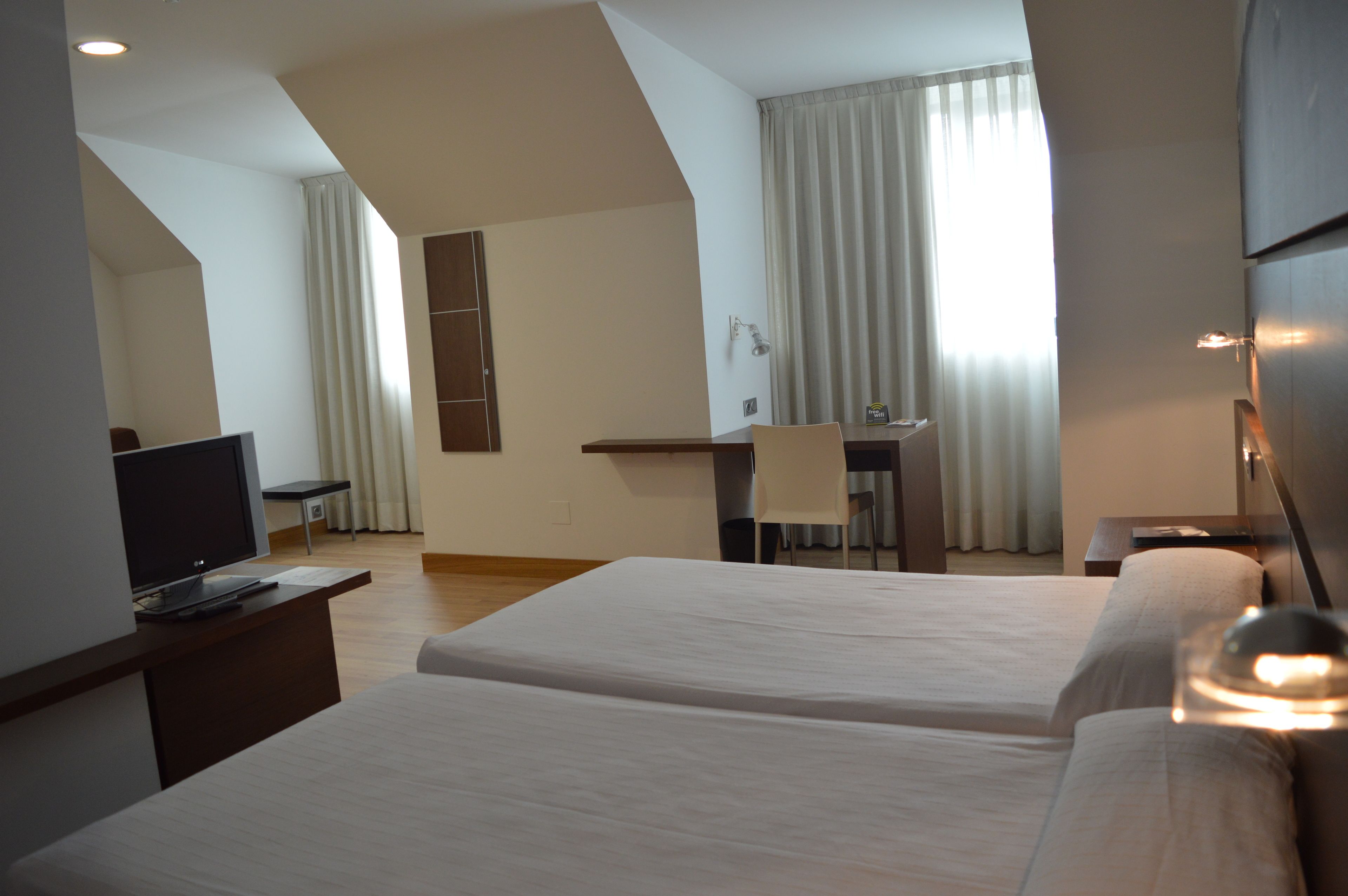 Habitación de hotel con dos camas, un escritorio, una silla, un televisor y una ventana con cortinas.
